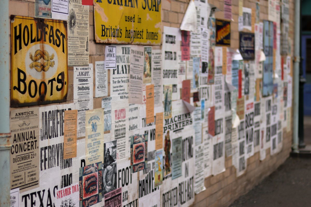 A brick wall covered with vintage posters, advertisements, and notices in various colours, some peeling at the edges.